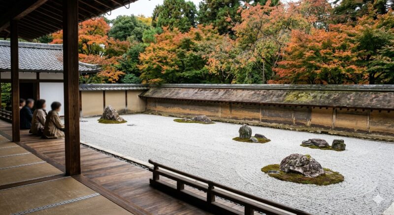 A serene Zen rock garden (karesansui) at Ryoan-ji Temple, with gravel, mossy rocks, an earthen wall, and autumn foliage, viewed from a wooden veranda.
