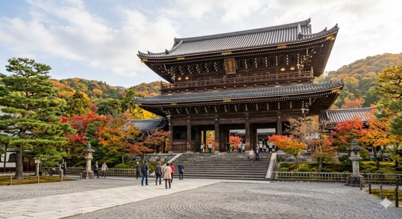 A wide-angle, realistic photograph of the majestic wooden Sanmon Gate of a large Japanese temple, set within a meticulously raked gravel courtyard. The two-story gate features traditional tiled roofing and a prominent golden plaque with Japanese characters. Steps lead up to the entrance, where small, respectfully dressed visitors are walking. The scene is surrounded by vibrant green, red, and orange maple and pine trees in peak autumn color, with foliage-covered hills rising behind the temple. Traditional stone lanterns and fences line the paved path.